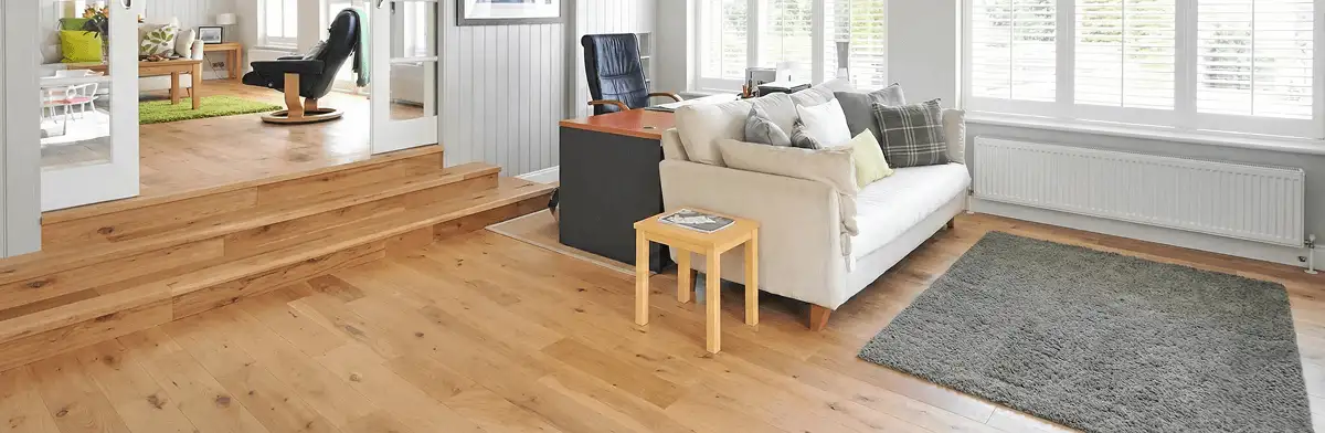 A modern living room with professionally installed laminate flooring, a beige sofa, a small side table, a gray rug, and large windows with white shutters in Lincoln, NE